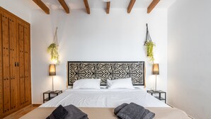 Une chambre d’hôtel avec un lit, deux tables de chevet, une armoire en bois et des plantes suspendues.