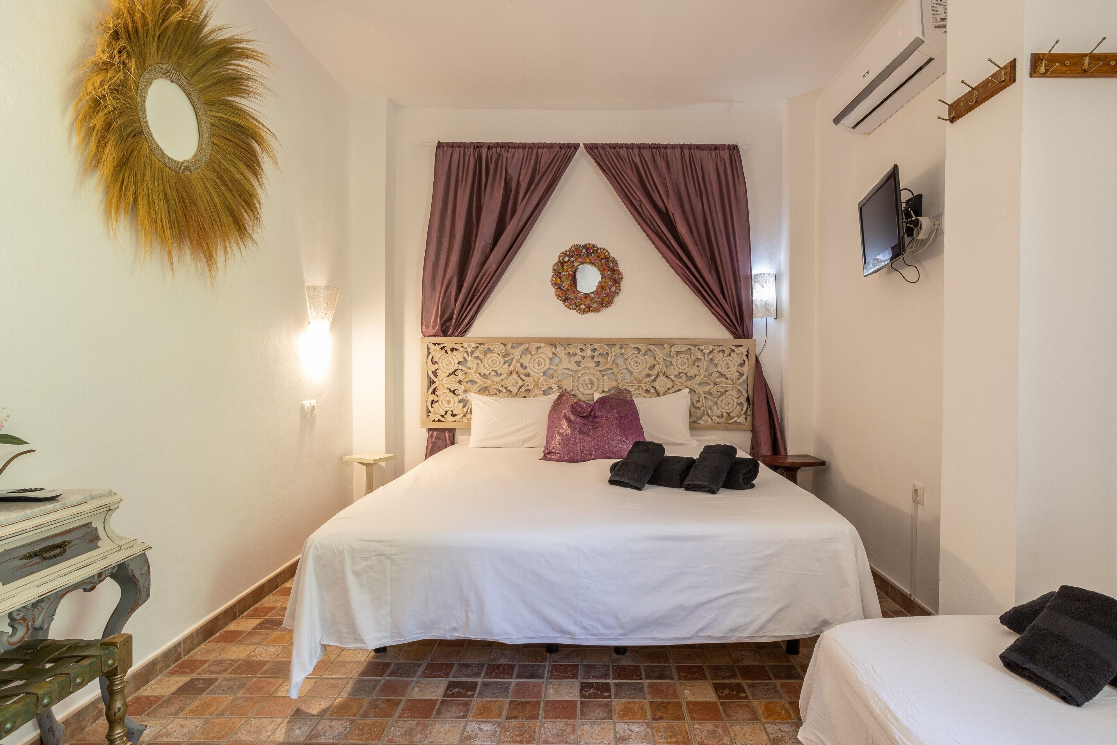 Un dormitorio con cama, mesita de noche, espejo, televisor de pared y decoración en la pared.