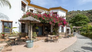 A building with a patio area featuring outdoor seating, a thatched umbrella, and potted plants. - Holiday Home 'Finca Arrijana' with Mountain View, Wi-Fi and Air Conditioning (Sayalonga)