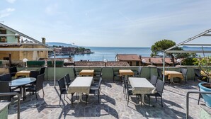 Terraza al aire libre con mesas y sillas, con vistas a una masa de agua y una costa distante.