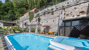 Una piscina con un muro de piedra y un edificio de techo rojo al fondo.