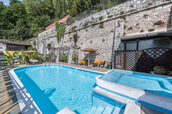 A swimming pool with a stone wall and a red-roofed building in the background.