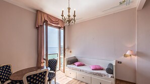 Una habitación con cama, una mesa de comedor con sillas, una araña y vista al mar.