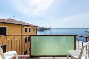 Un balcone con vista sul mare, un edificio giallo e una sedia bianca.