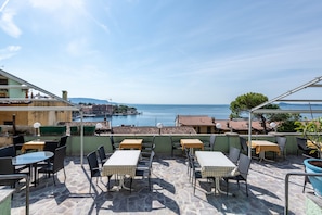 A terrace with tables and chairs, overlooking a body of water and buildings. - Hotel Apartment "Gardasol Romantic 1 Vista Lago" with Lake View, Pool & Wi-Fi (Toscolano maderno)