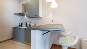 Ett modernt kök med grå skåp, en rostfri köksfläkt, en vattenkokare, en kaffebryggare och ett vitt handfat på en piedestal.