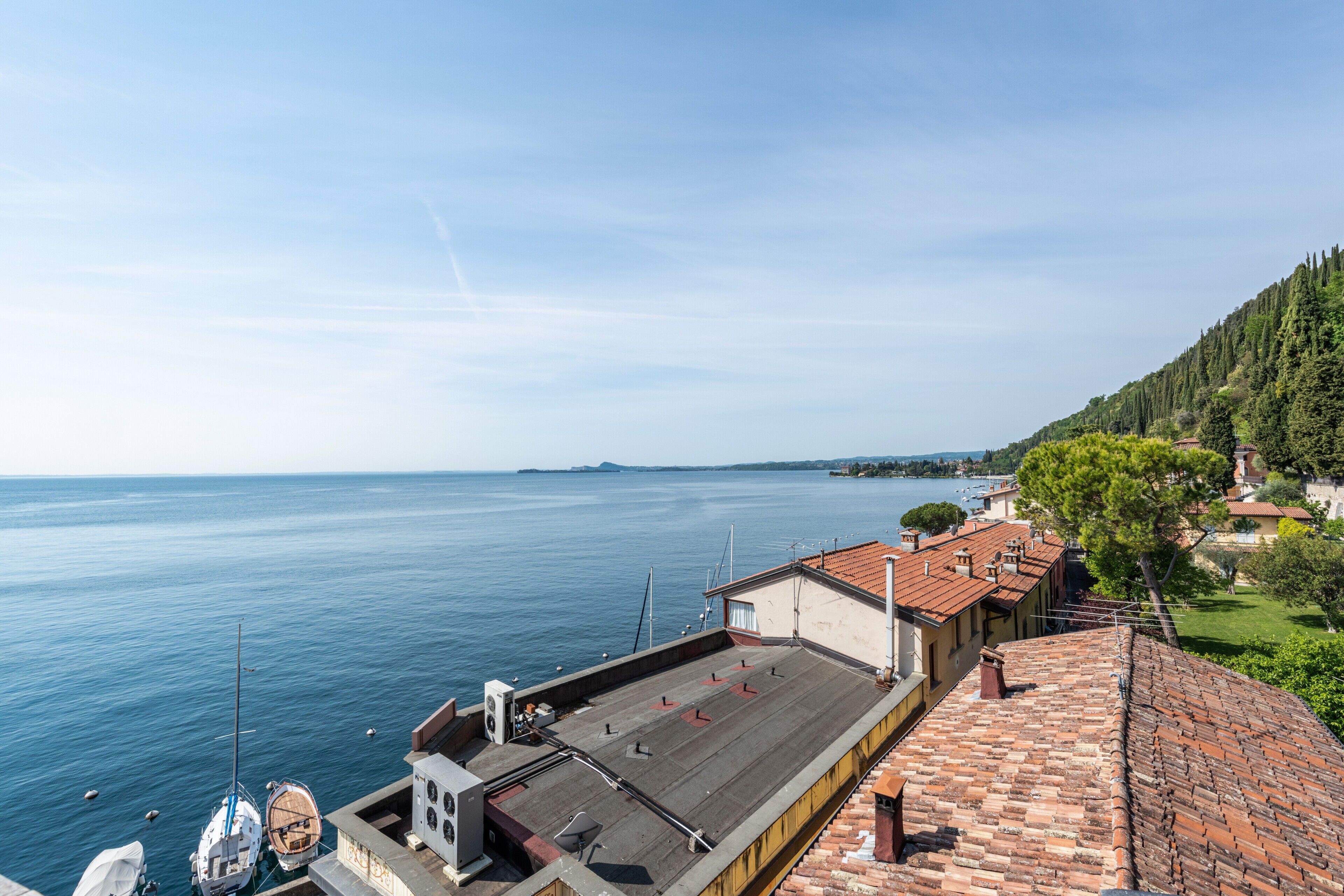 A coastal view with a rooftop terrace, boats, and buildings along the shoreline.