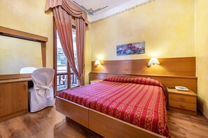 A hotel room with a wooden bed, a desk, a chair, a nightstand, and a window with curtains.