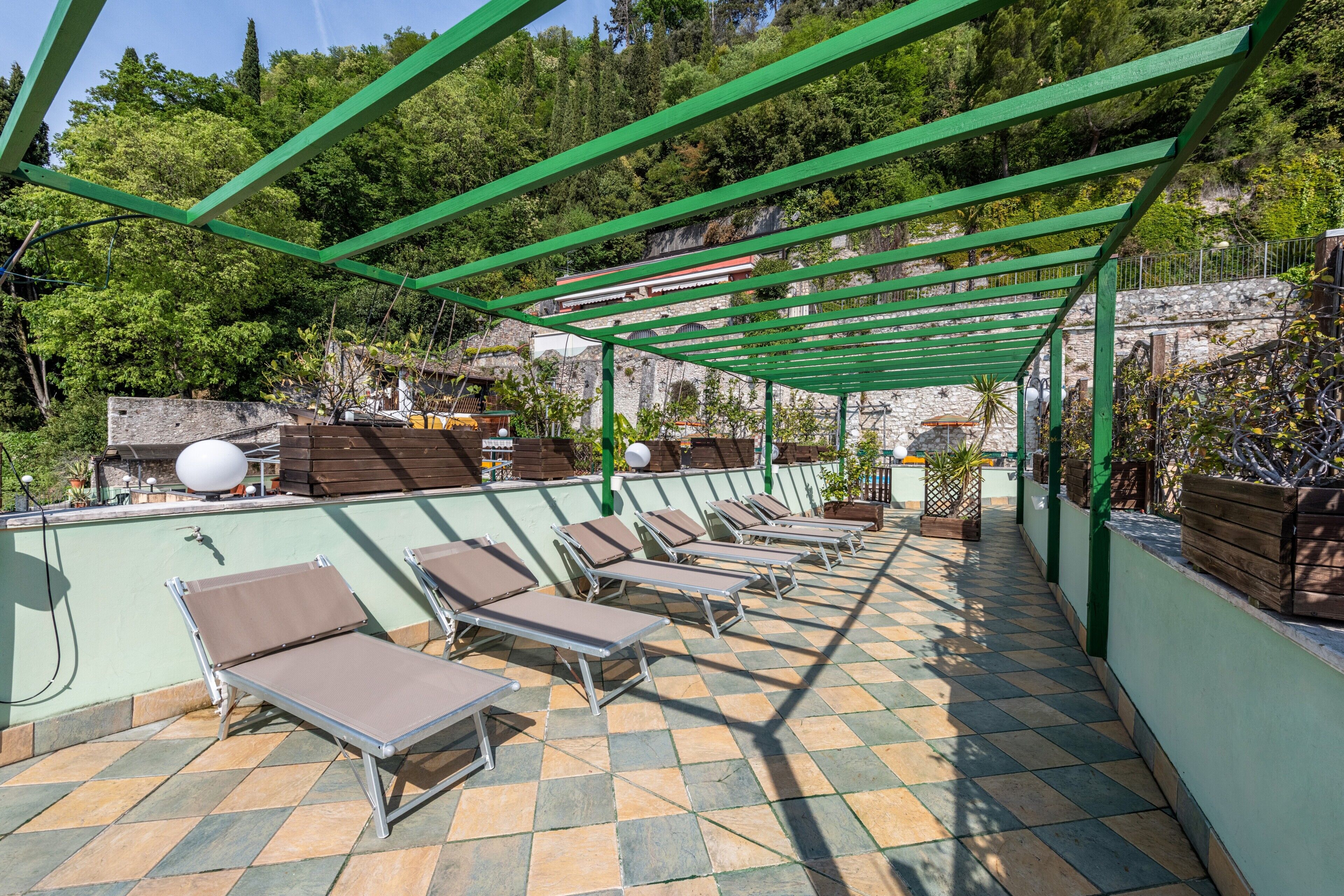 Terraço no telhado com espreguiçadeiras, uma pérgula verde e piso xadrez.
