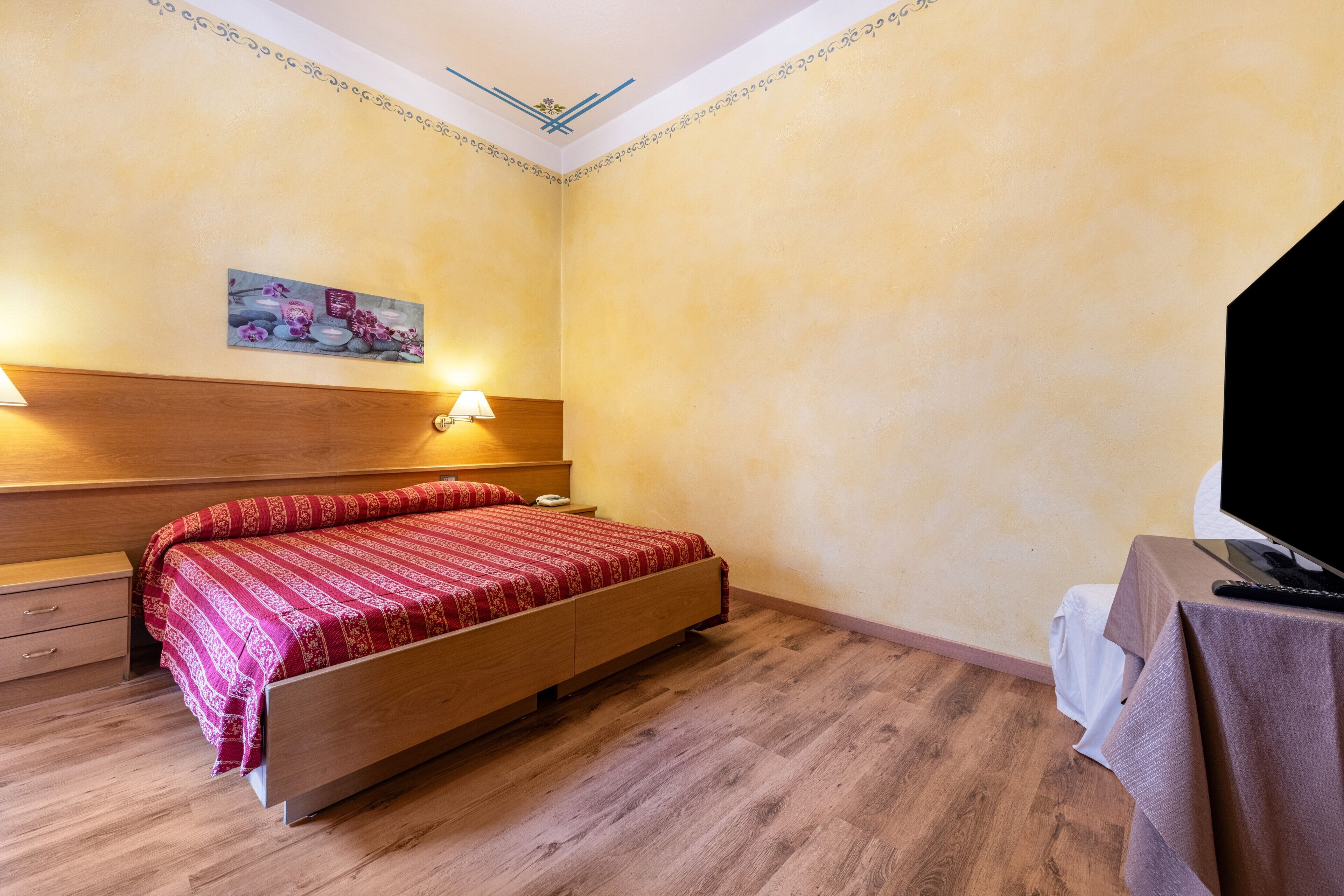 Una camera da letto con un letto di legno, lampade sui comodini, un quadro appeso al muro e una televisione su un tavolino.