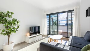Una sala moderna con un televisor de pantalla plana, un sofá, una mesa de comedor y un ventanal con vistas a la ciudad.