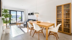 Un comedor moderno con una mesa de madera, sillas blancas, una lámpara colgante y vistas de la ciudad a través de amplias ventanas.