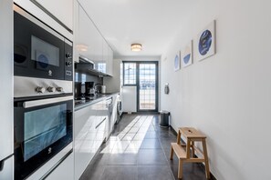 A modern kitchen with a built-in oven, a washing machine, and a wooden stool.