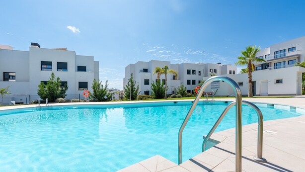 Una piscina con barandales metálicos, rodeada de edificios modernos y palmeras.