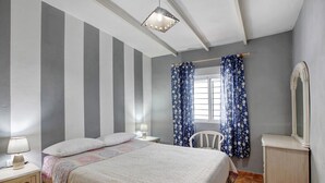 Een slaapkamer met een bed, nachtkastjes, een stoel, een garderobe en een raam met gordijnen.