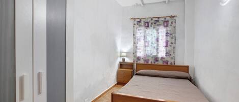 A bedroom with a bed, a wardrobe, a nightstand, a lamp, and a curtain.
