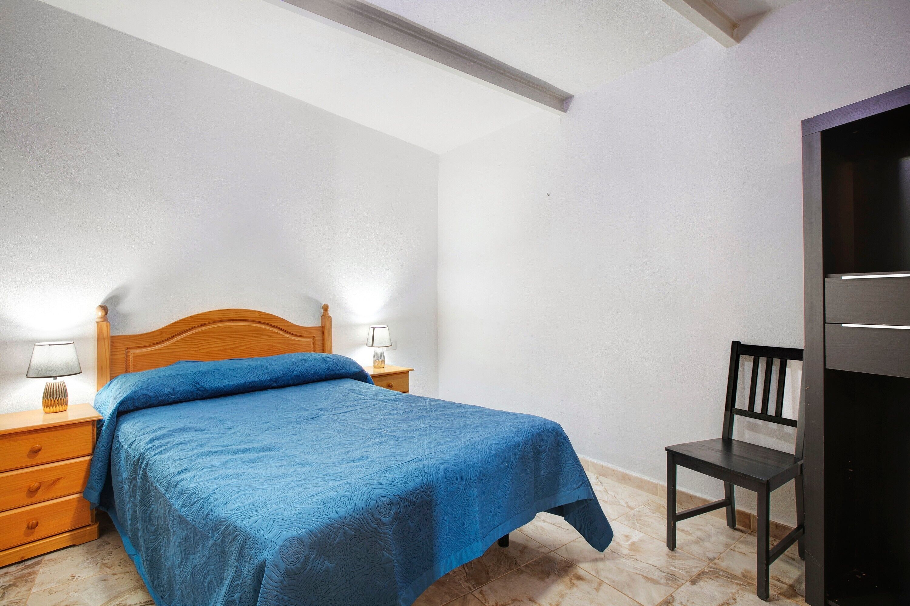 A bedroom with a bed, bedside lamps, a wooden nightstand, a chair, and a wardrobe.