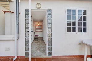 A hallway with a tiled floor, a chair, a wall-mounted light fixture, and a window with a view.