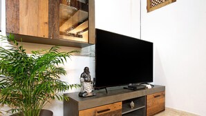 A flat-screen TV on a wooden and metal TV stand, a potted plant, and a statue. - Vacation Home "Casa Alexis" with Wi-Fi, Terrace & Garden (La lajita)