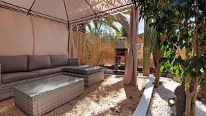 A covered outdoor seating area with a sofa and a glass-top table, surrounded by pebbles and plants. - Vacation Home "Casa Alexis" with Wi-Fi, Terrace & Garden (La lajita)
