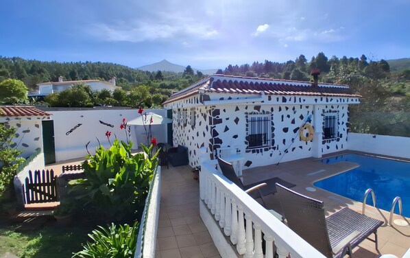 A poolside area with a white building featuring a cow print pattern, a pool, and a view of a mountain.