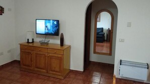 Una sala de estar con un mueble de madera, un televisor de pantalla plana y piso de baldosas.