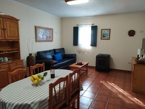 A living room with a sofa, a dining table with chairs, a TV, a fireplace, and a kitchen area with cabinets.