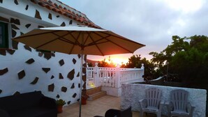 Un patio con mobiliario exterior, una pared blanca con un diseño único y vistas al atardecer.
