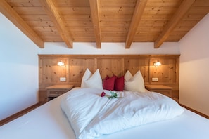 Une chambre avec un plafond en bois, un lit avec une literie blanche, des oreillers rouges et blancs, et des lampes de chevet.