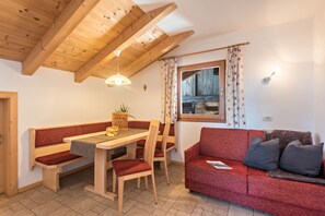 Une pièce chaleureuse avec un plafond en bois, une table à manger avec des chaises, un canapé rouge et une fenêtre avec des rideaux.