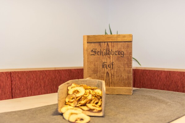Une enseigne en bois portant l’inscription « Schilbergh Hof », une boîte en bois contenant des tranches de pommes séchées, et un mur aux couleurs rouge et beige.