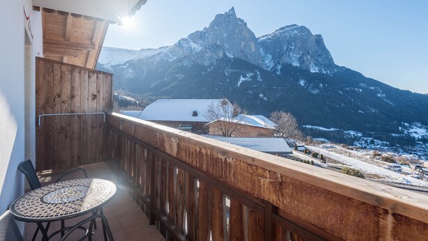 Ein Balkon mit Holzwertung, einem runden Tisch und Blick auf schneebedeckte Berge.