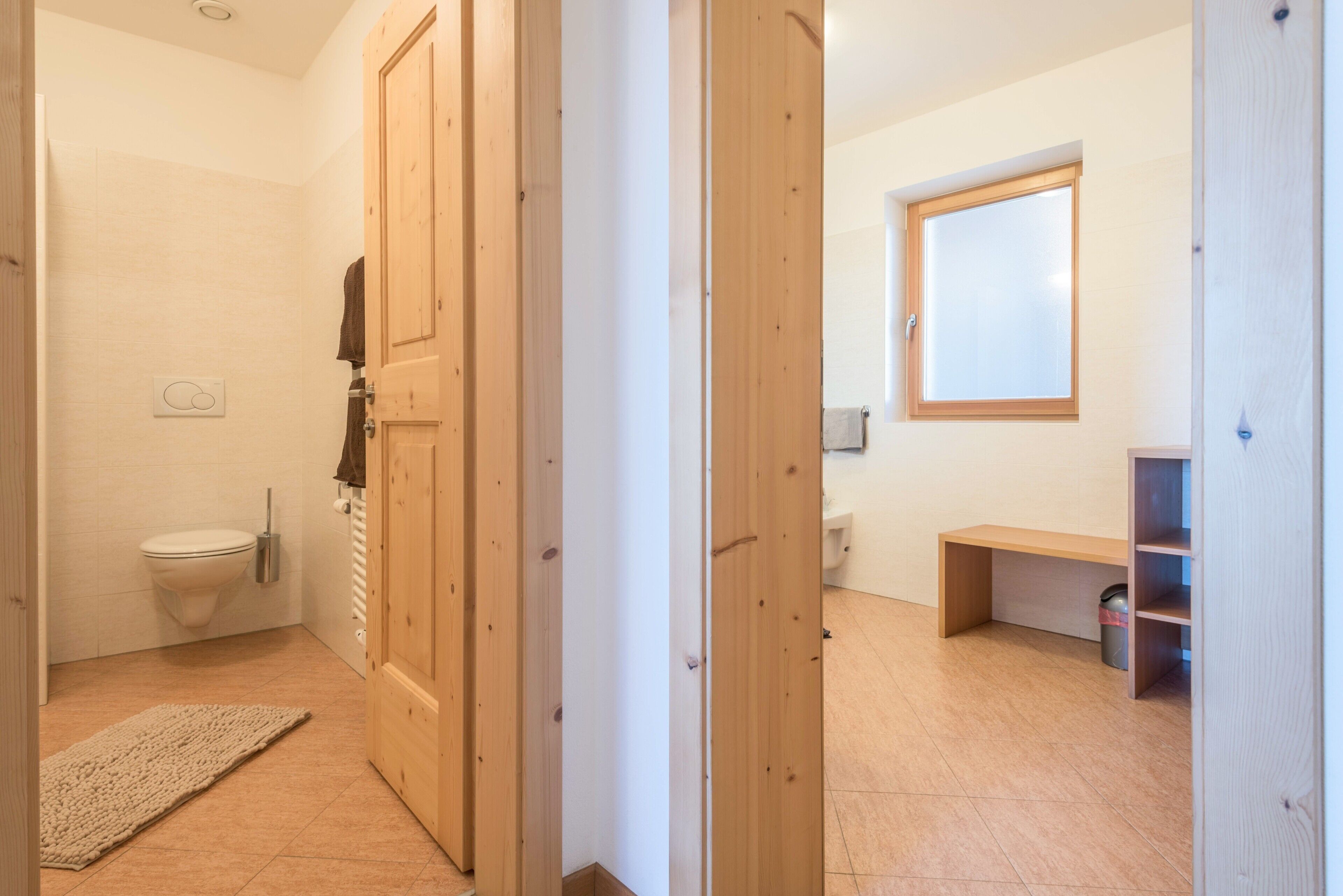 Ein Badezimmer mit Toilette, einer Holztür, einer Sitzbank und einem Fenster.