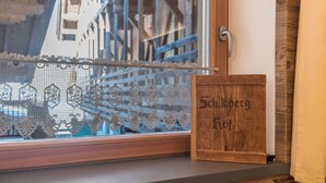 Ein Fenster mit Spitzenvorhängen, eine Holzschild mit der Aufschrift 'Schilberg Hof' und eine Holztür mit Griff.