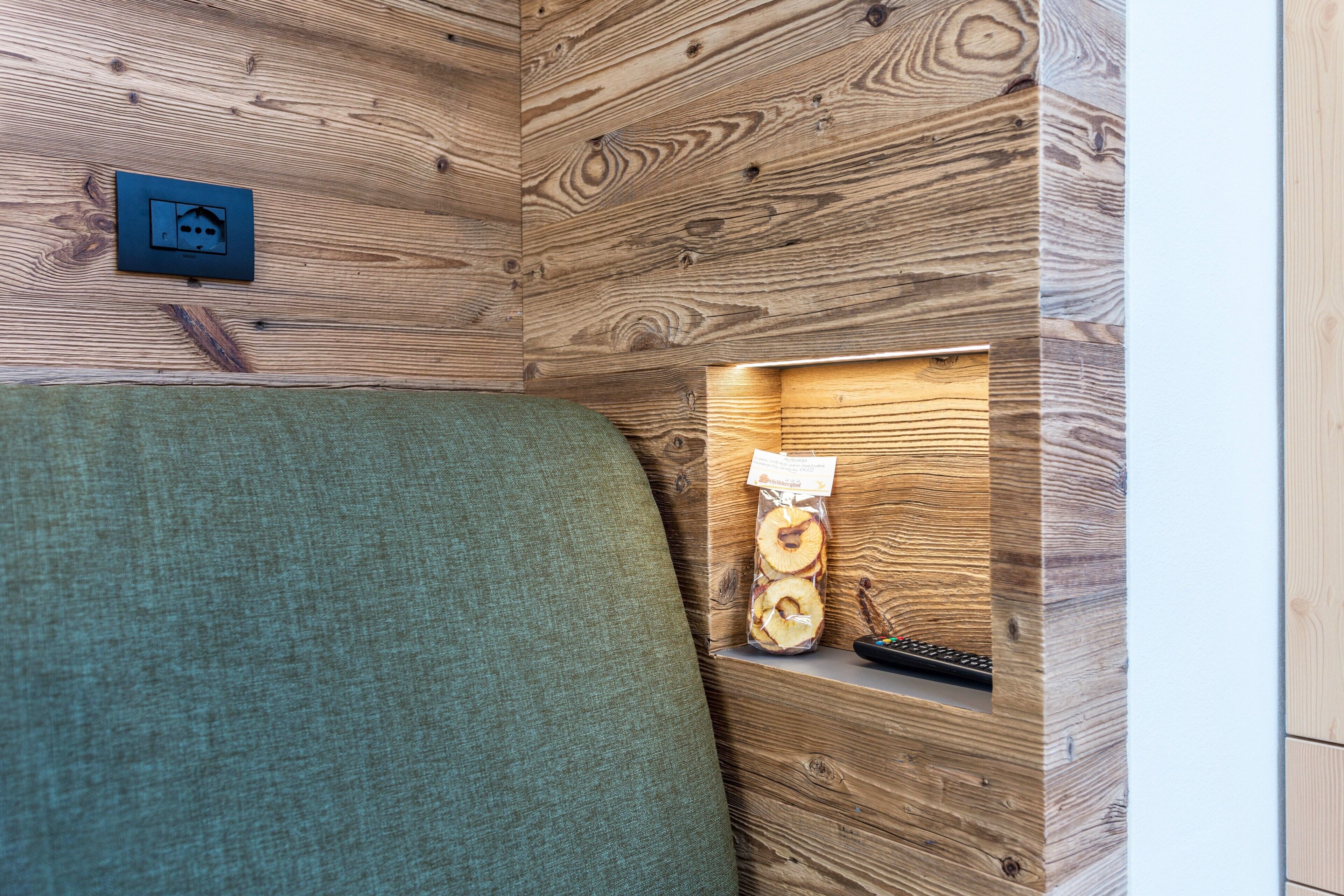 A wooden wall with a power outlet and a remote control on a shelf.