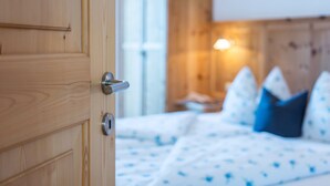 Una puerta de madera con un picaporte de metal, una cama con ropa de cama blanca y almohadas azules, y un aplique de pared.