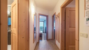 A hallway with wooden doors, a tiled floor, and a view into a room with a bed and a balcony.