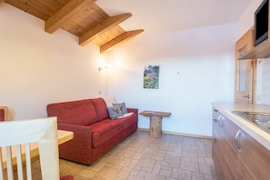 A compact living space with a red sofa, a small wooden table, a kitchen area with a sink, and a mounted TV.