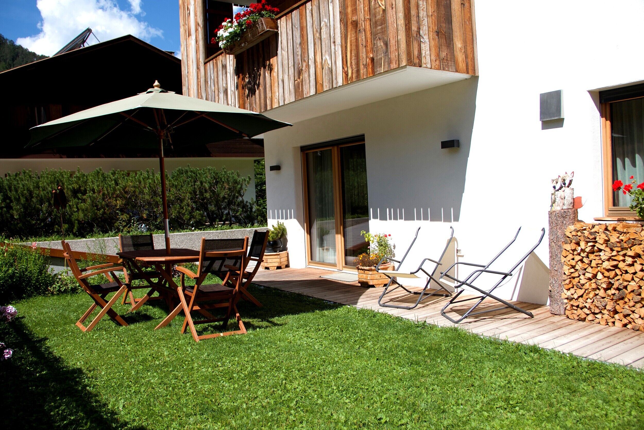 Ein modernes Haus mit einer Holzterrasse, Gartenmöbeln und einem Garten.