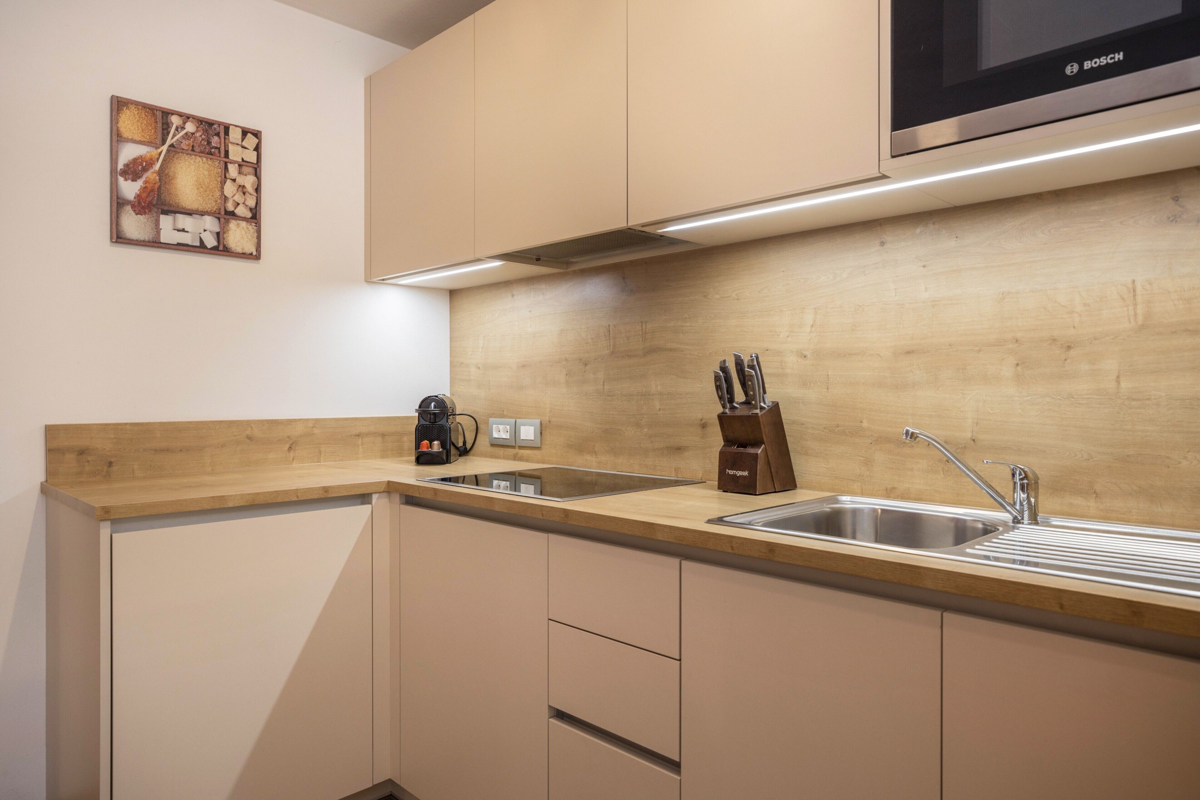 Une cuisine moderne dotée d’un plan de travail en bois, d’un évier en acier inoxydable, d’un four à micro-ondes Bosch et de couteaux suspendus.