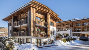A multi-story wooden building with balconies, a ski slope in the background, and snow on the ground. - Apartment 'Ciasa Rungg App Corones' with Mountain View, Garden & Wi-Fi (St.Vigil)