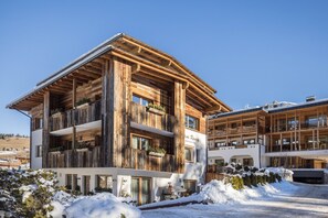 Ein mehrstöckiges Holzgebäude mit Balkonen, im Hintergrund eine Skipiste und Schnee auf dem Boden.