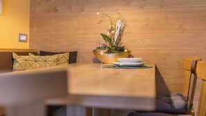A dining area with a wooden table, chairs, a bowl with a plant, and a wine glass. - Apartment 'Ciasa Rungg App Corones' with Mountain View, Garden & Wi-Fi (St.Vigil)
