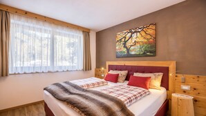 A double bed with a red headboard, two bedside tables, a painting of a tree, and a window with sheer curtains. - Apartment 'Ciasa Rungg App Corones' with Mountain View, Garden & Wi-Fi (St.Vigil)