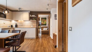 Une cuisine moderne avec des meubles en bois, un coin repas comprenant une table et des chaises, et un couloir menant à un espace de vie avec un canapé et un tableau.