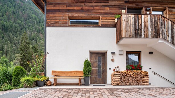 Un balcon en bois au design rustique, un banc en bois, une porte et une vue sur une montagne boisée.