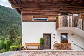 Uma varanda de madeira com design rústico, um banco de madeira, uma porta e vista para uma montanha arborizada.