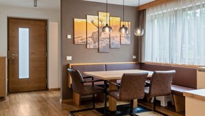 Un coin repas comprenant une table en bois, des chaises rembourrées de couleur marron, un banc et une œuvre d’art accrochée au mur.