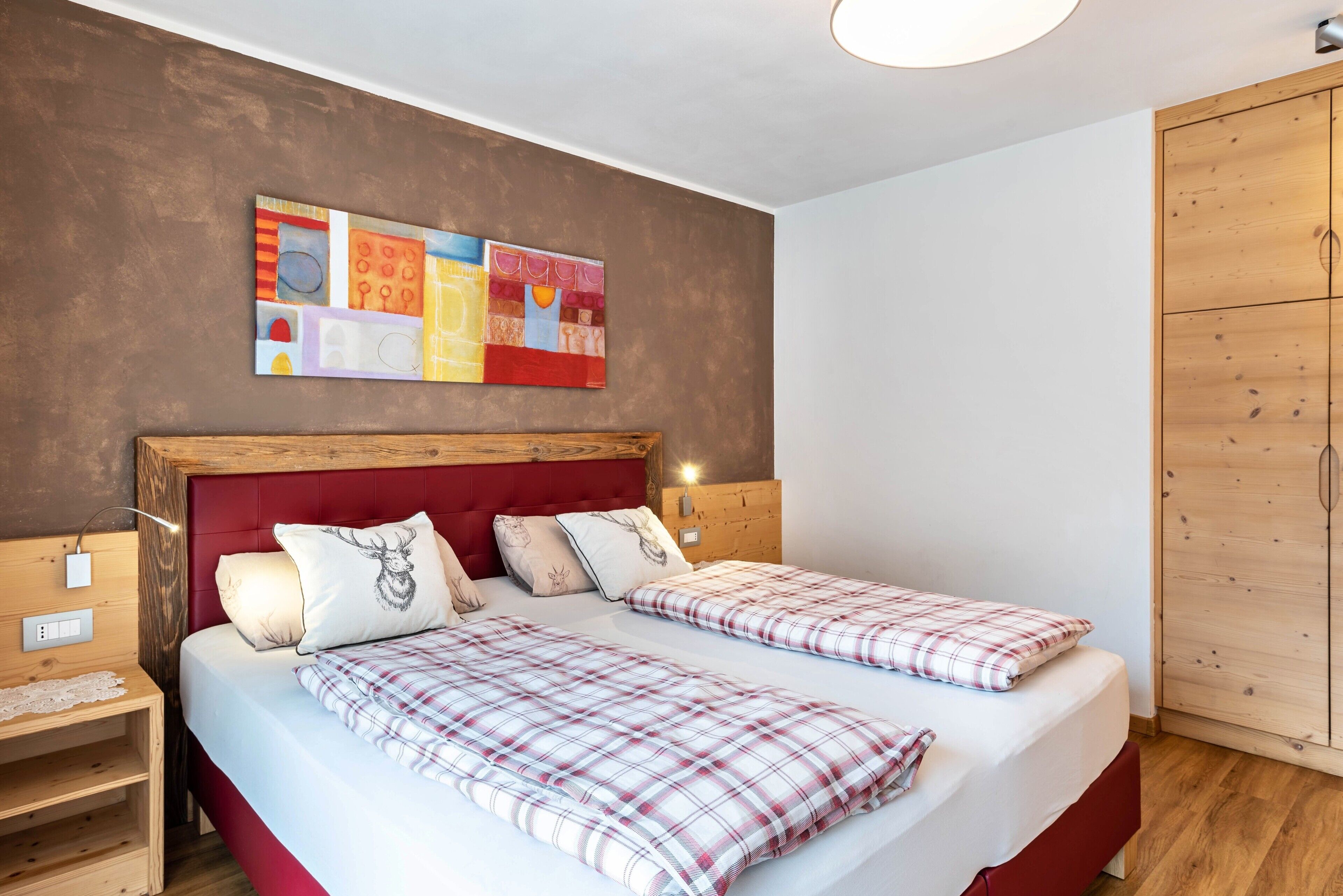 Ein Doppelbett mit kariertem Überwurf, einem roten Kopfteil und einem an der Wand hängenden abstrakten Gemälde.