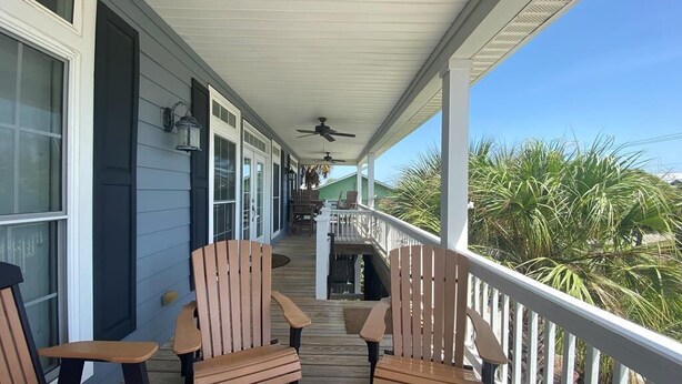 Un portico coperto con sedie e tavolo in legno, una ventola a soffitto e vista su palme.